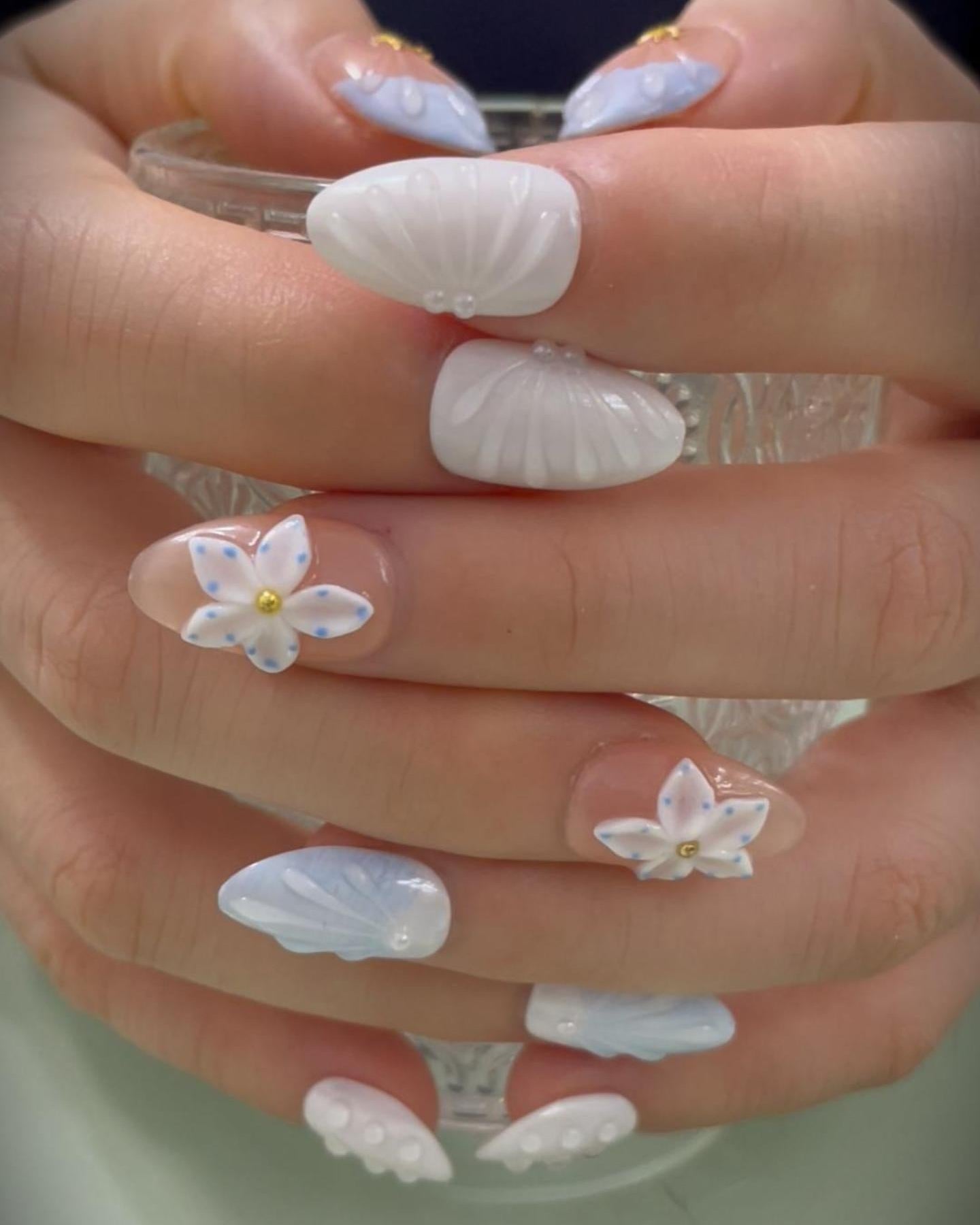 Ocean Bloom Press-On Nails both hands holding clear glass — short almond nails with 3D gold starfish, white sculptural texture, blue flower with pearl center, aurora shimmer design | MOONLEE