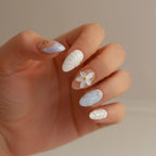 Ocean Bloom Handmade Press-On Nails close-up — short almond shape, nude base with lavender-blue diagonal marble and gold starfish charm on thumb, white 5-petal flower on middle finger, light blue aurora texture on ring finger, pearl dot pinky | MOONLEE