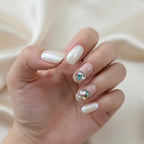 Close-up of a hand wearing Gemstone Glow handmade press-on nails — pearlescent white nails on thumb, middle, and pinky fingers; sheer nude
