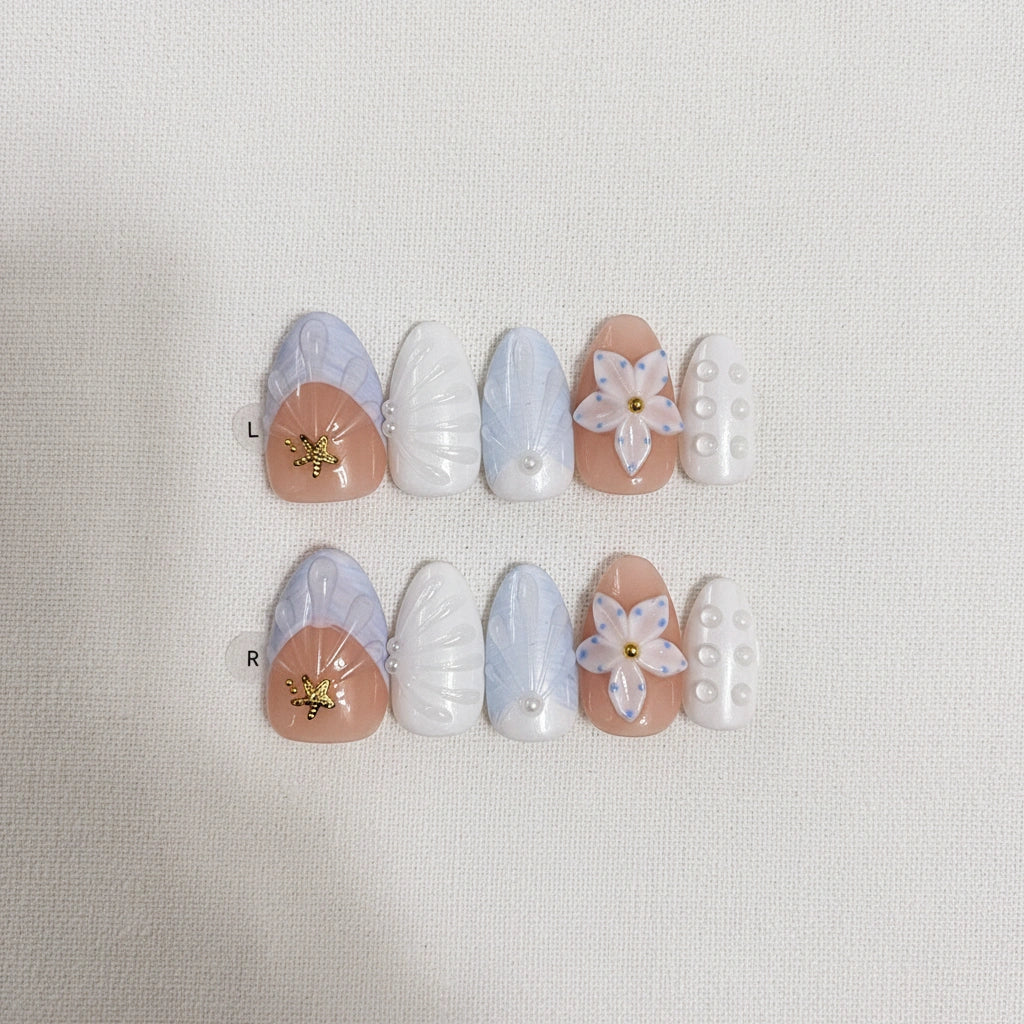 Ocean Bloom  Handmade Press-On Nails flat lay display — 10 pieces in two rows showing left and right hand set, short almond shape with lavender-blue marble, gold starfish charm, white 5-petal flower, pearl dot accents on white linen background | MOONLEE